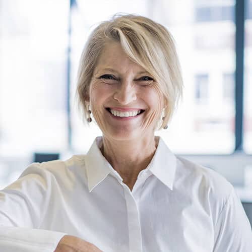 Smiling middle-aged woman in white blouse indoors.